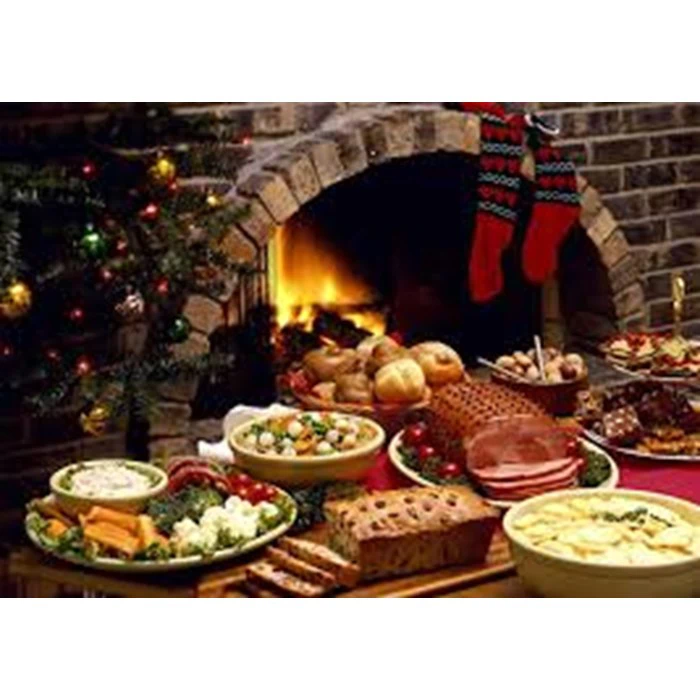 Et festligt julemåltid med forskellige retter, brød, skinke, ost og frugt foran en pejs med strømper og et pyntet juletræ.